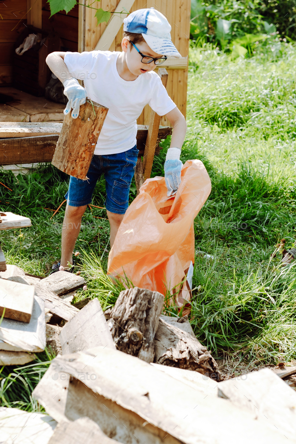 the boy collects garbage in a bag. The child will help with cleaning the territory on the street