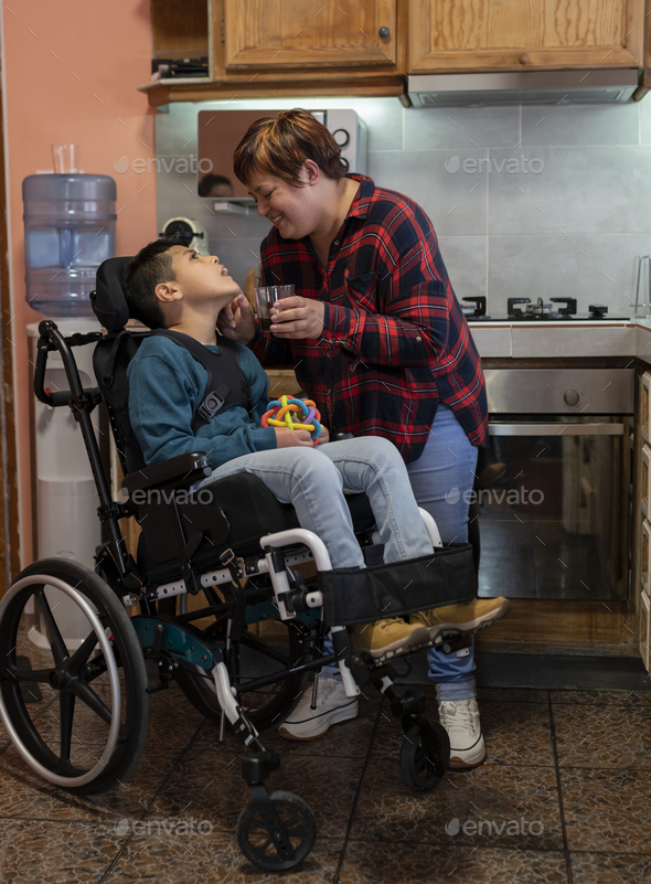 Mother Caring For Her Wheelchair Bound Disabled Son In The Kitchen Concept Disability Stock