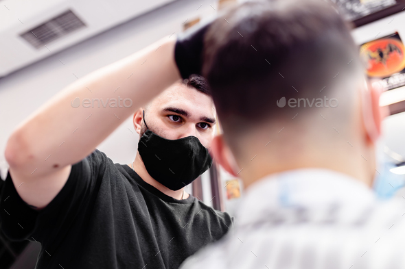 Men\'s haircut in a barbershop. Client and barber in anti-virus masks.