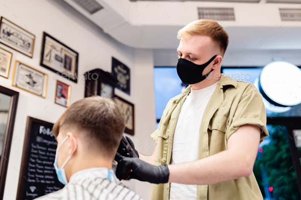 Men\'s haircut in a barbershop. Client and barber in anti-virus masks.
