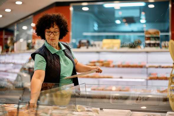 Female worker checking products in freezer while working in supermarket. - Stock Photo - Images
