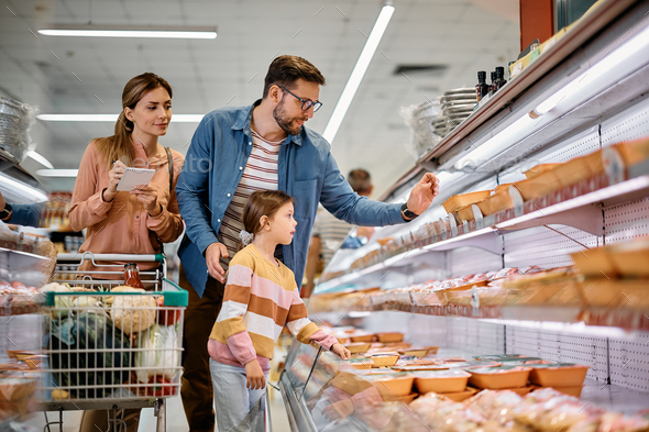 Young family buying food at refrigerated section in supermarket.