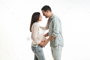 pregnant woman and husband standing looking into each other's eyes and touching each other's belly