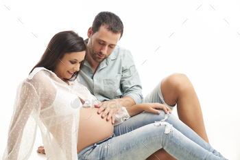 pregnant woman and her husband sitting smiling, looking at and touching her belly