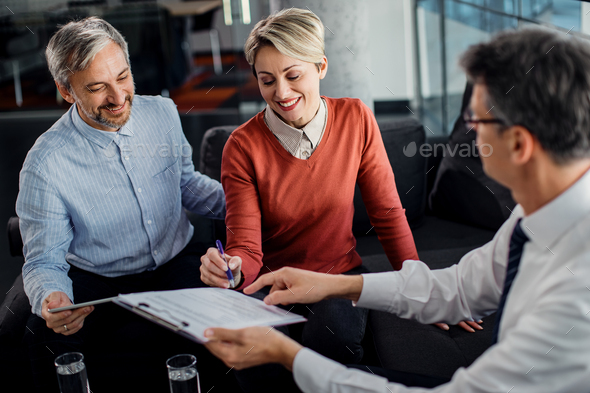 Happy couple signing lease agreement with their agent during a meeting in the office. - Stock Photo - Images