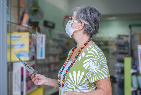 Senior woman wearing mask in pharmacy store looking at medical products