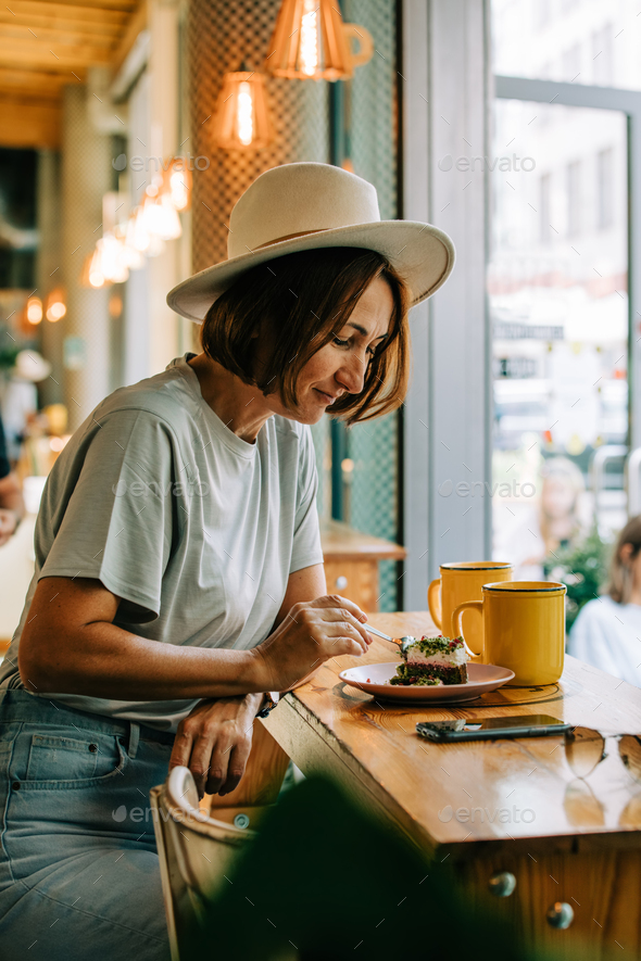 stylish fifty-year-old woman drinking coffee and eats cake in a cafe - Stock Photo - Images