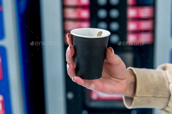 Woman holds paper coffee cup by vending machine