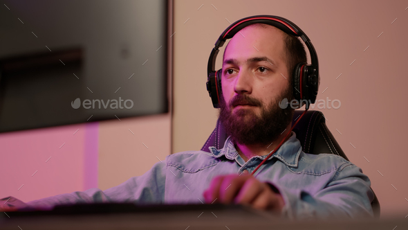 Handheld shot of man with gaming headset looking at computer screen and talking to team members