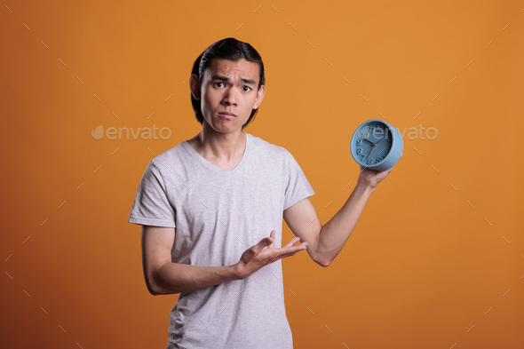 Young asian man running late, holding alarm clock