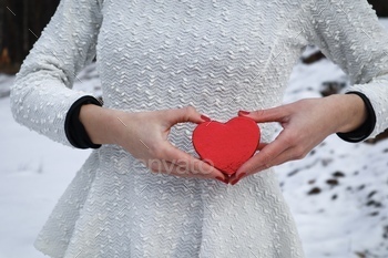Pregnant woman holding a red heart in her hands in front of her belly
