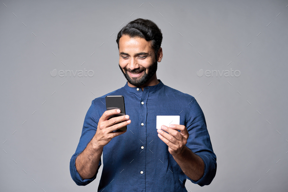 Happy indian business man holding phone and credit card using mobile bank app.