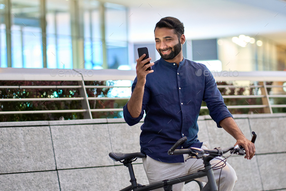 Indian man using phone using bike rental app renting bicycle in city park.
