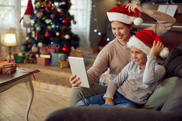Playful mother and son taking selfie with touchpad on Christmas day at home.