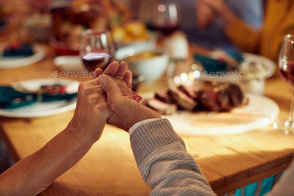Close-up of senior couple saying grace during Thanksgiving meal with family at dining table.