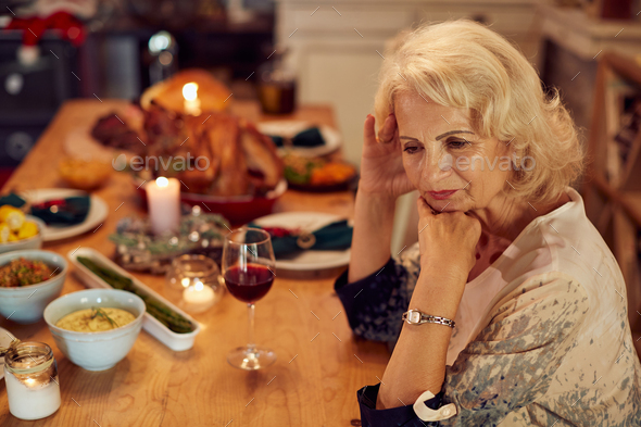 Senior woman feeling sad while sitting alone at dining table on Thanksgiving.