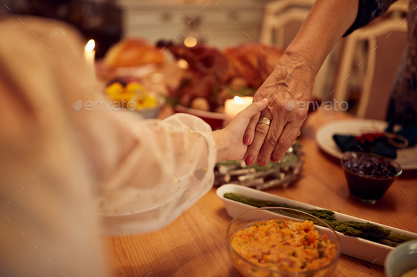 Close-up of mother and daughter holding hands while praying during Thanksgiving lunch.