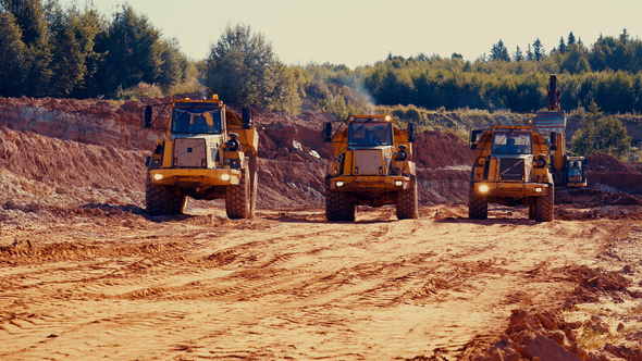 3 dump trucks driving out of red clay quarry.