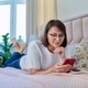 Middle aged relaxed woman lying on bed at home using smartphone - PhotoDune Item for Sale