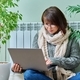 Woman in warm sweater using laptop sitting near heating radiator at home - PhotoDune Item for Sale