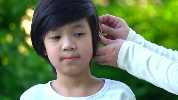 Mother Inserting Hearing Aid In The Ear Of Her Son alt