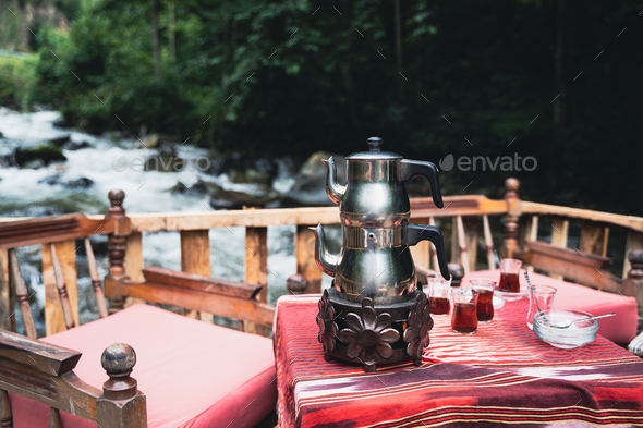 traditional Turkish tea chrome kettle and glasses on a restaurant table with chairs near a river