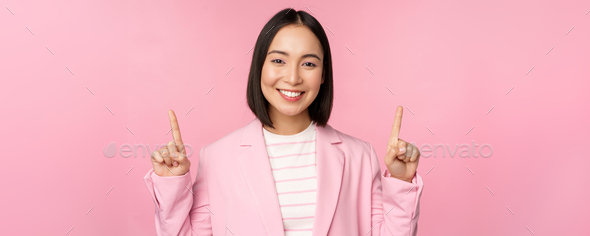 Portrait of asian businesswoman pointing fingers up and smiling, showing business company logo