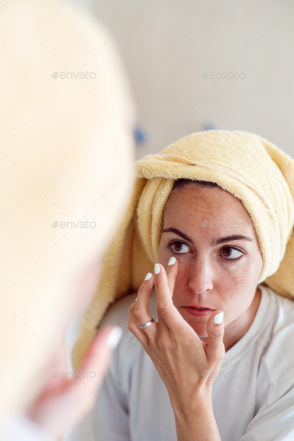 woman in towel after shower look in mirror apply moisturizing facial