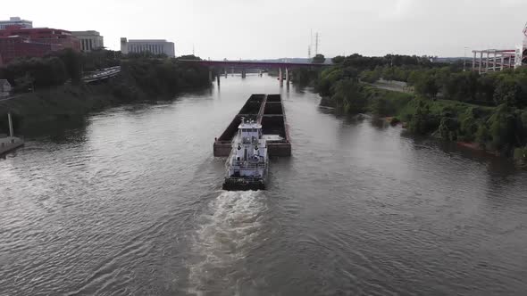 Tugboat pushes and guides large commercial transport barge on river by downtown Nashville city, Illi alt
