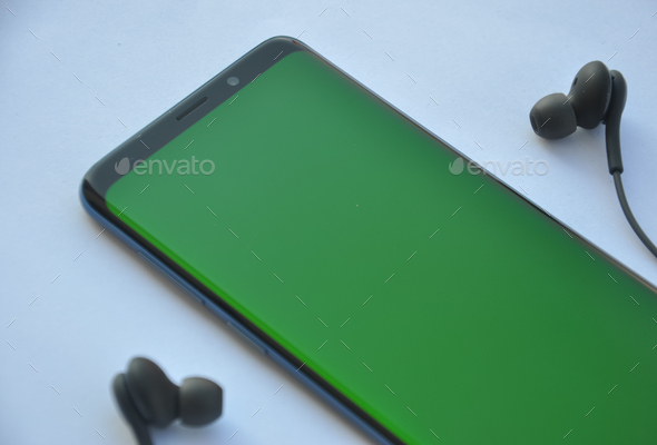 Low angle view of curved screen mobile phone with green screen and black color earphone