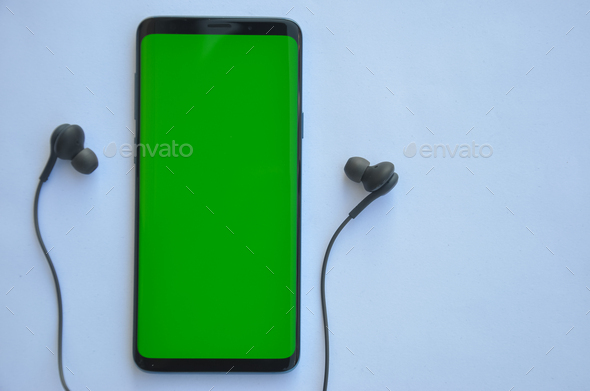 High angle shot of smartphone phone with green screen and black color earphone
