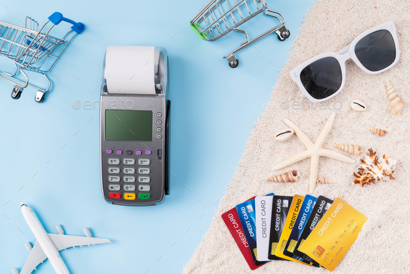 Top view of credit cards and card reader machine with invoice bill and starfish, sunglasses on sand.