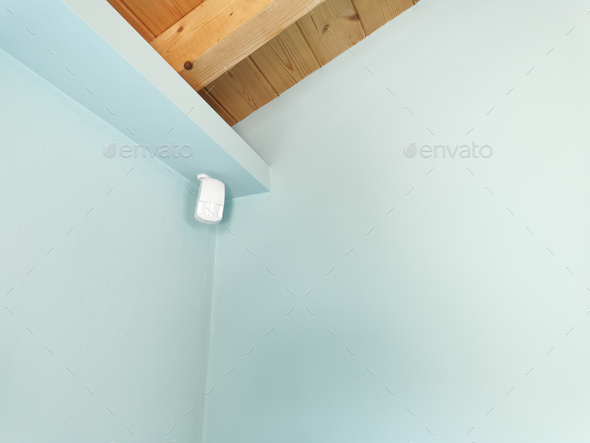 Motion sensor or detector for security system mounted on blue wall in room with wooden ceiling