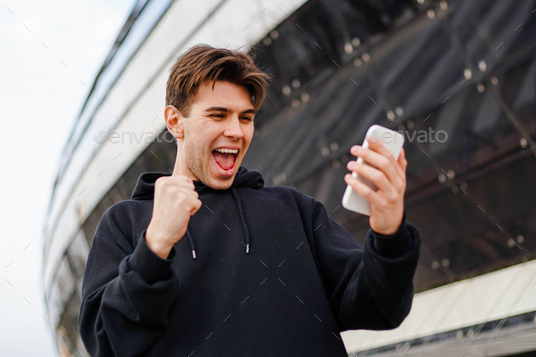 Cheerful man holding smartphone and celebrate win a bet. Soccer bet, sports gambling.