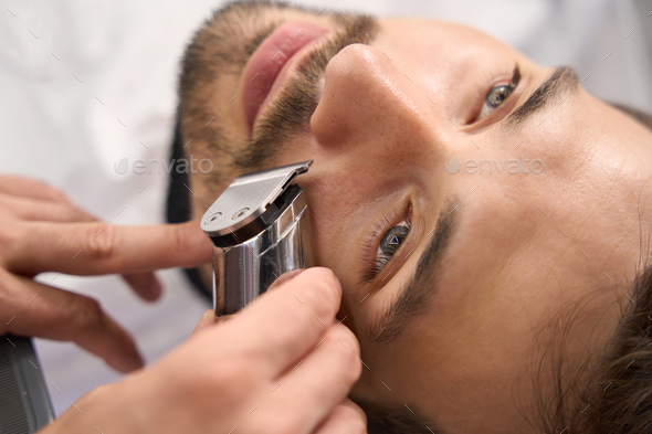 Serious man not moving while barber trimming his moustache