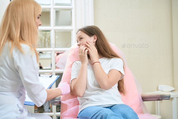 Teenage girl points her hand to her cheek to beautician