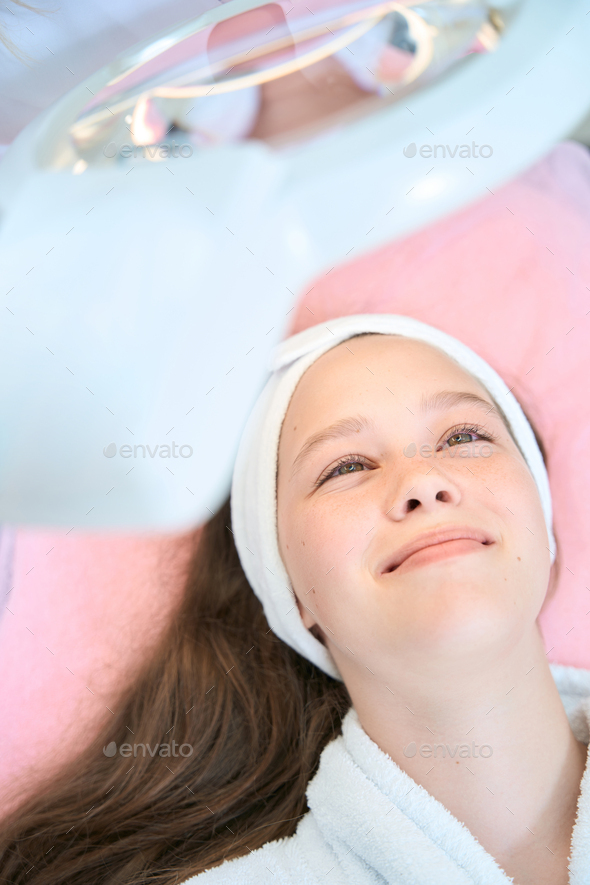 Photo of face of smiling girl lying under magnifying lamp