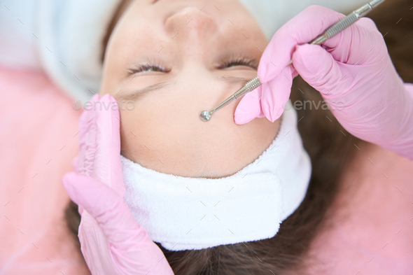 Beautician cleans girl forehead with uno spoon in cosmetology clinic - Stock Photo - Images