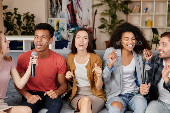 Music brings joy. Enthusiastic multicultured friends singing with microphone while playing karaoke