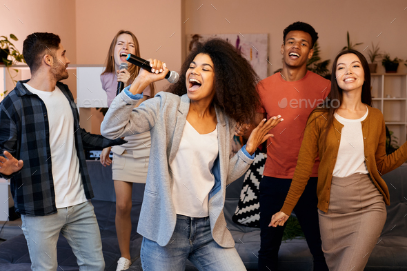 Singing means happiness. Pretty mixed race girl looking enthusiastic while holding microphone and - Stock Photo - Images