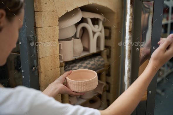 Craftswoman holds vase in hands, she sends it kiln for firing