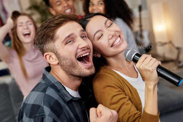 Bring the song to life. Young excited couple or friends holding microphone and singing together