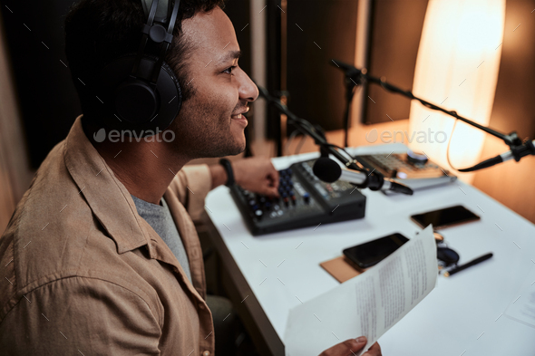 Portrait of young male radio host going live on air, talking in microphone, holding a