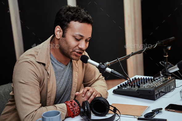 Portrait of young male radio host going live on air, talking in microphone, reading a