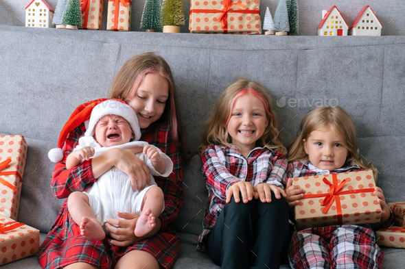 Four sisters with infant little brother sitting on couch with gift boxes.