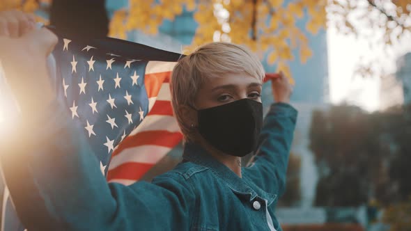 Young Caucasian Woman Dancing with Face Mask and American Flag in the Park. Election 2020 alt