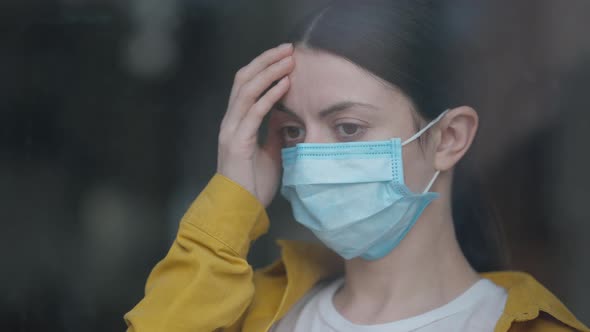 Headshot Portrait of Young Sad Caucasian Woman in Coronavirus Face Mask Standing Indoors Looking Out alt