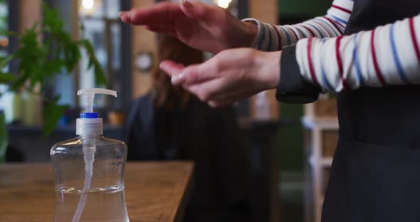 Mid section of female hairdresser sanitizing her hands at hair salon alt