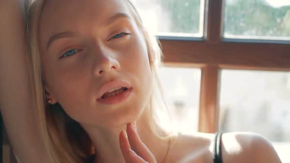 fashion portrait of a beautiful young woman with blue eyes and blonde hair poses near the window alt