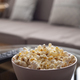 Bowl with popcorn and tv remote control on glass table near sofa - PhotoDune Item for Sale